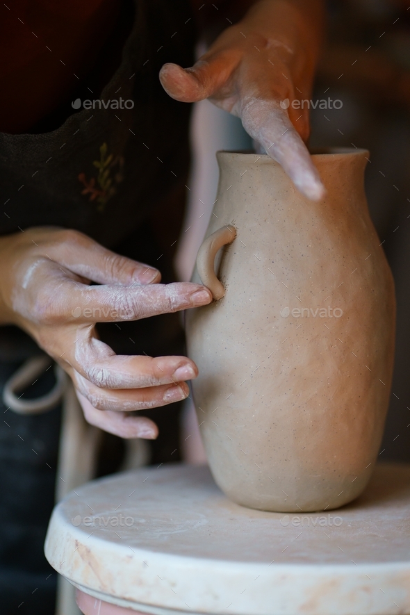 Working with raw clay: pottery master add details to potter vase jug. Artistic occupation in studio