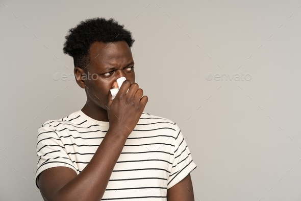 Sick african man suffering from seasonal allergy symptoms, ill black guy blowing nose in tissue