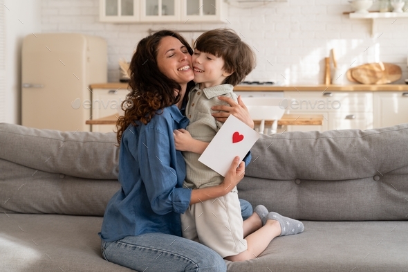 Adorable kid boy congratulate mom with mother day or birthday embracing ...