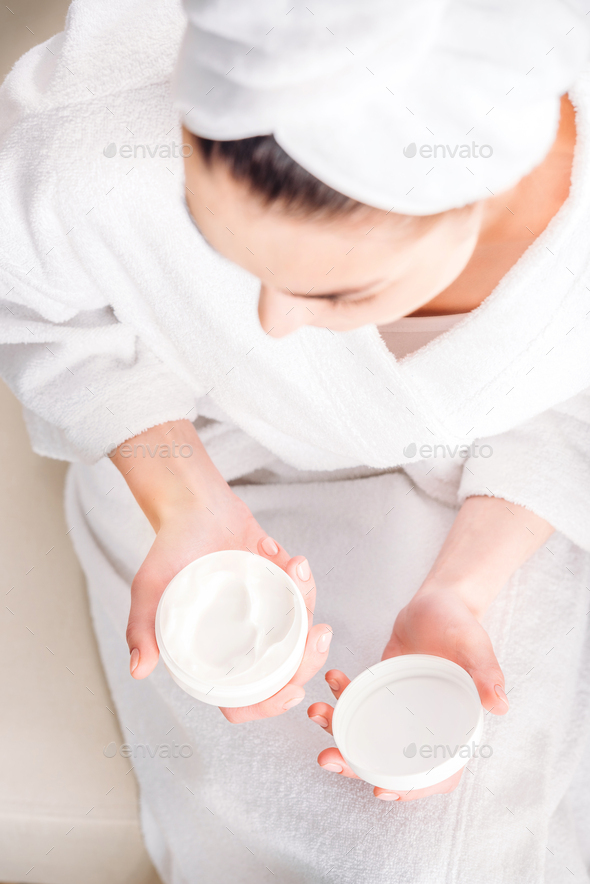 Overhead shot of woman in white bathrobe opening up a jar of face cream