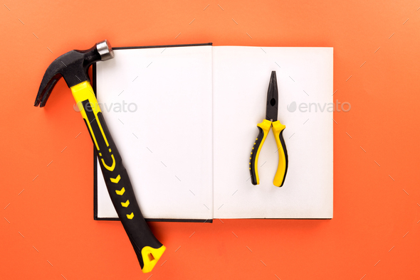 Top view shot of open book with blank pages, hammer and pliers on orange surface