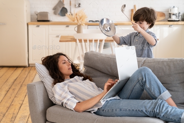 Kid disturb mom focused on laptop lying on couch. Calm mother browse pay no attention to loud boy
