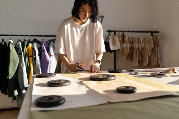 Woman tailor cut clothing samples of pattern drafts paper in garment factory design studio atelier