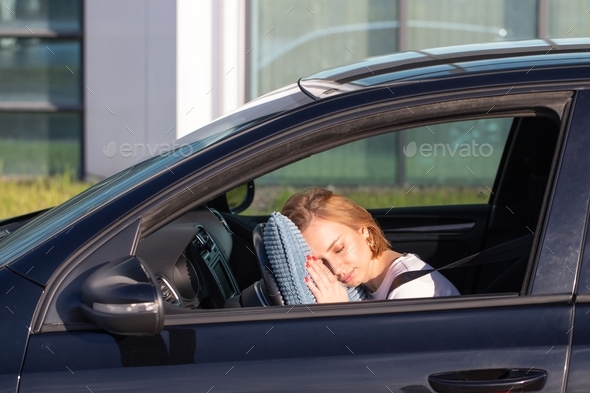 Tired female driver asleep on pillow on steering wheel, resting after long hours driving a car