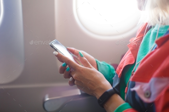 young woman uses a mobile phone. The girl reads an e-book from the phone on the plane.