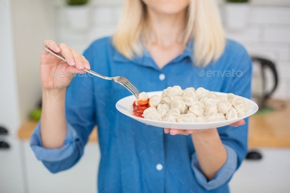 Beautiful young girl holding a large plate of delicious boiled dumplings (pelmeni) in her hands.