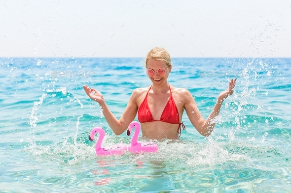 Young woman in the sea laughs and splashes water. Girl in a red swimsuit and pink glasses. Beach
