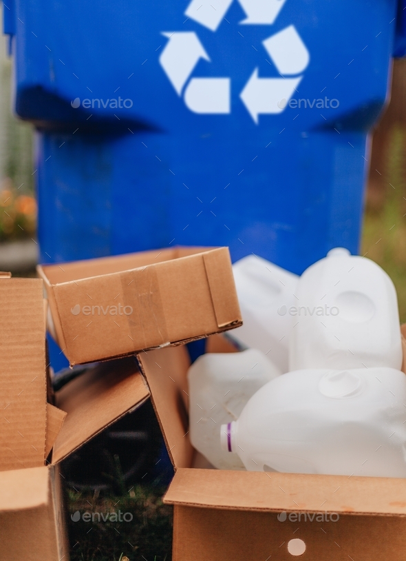Stack of cardboard boxes and plastic bottles next to a recycle bin
