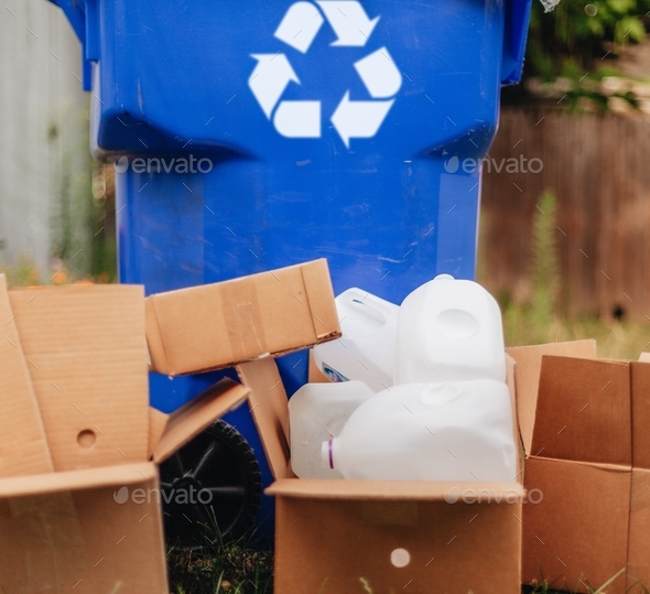 Cardboard boxes and plastic bottles next to blue recycling bin, eco friendly