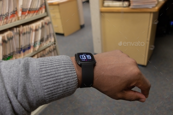 African American man in office setting looking at time on smart watch, Fitbit versa