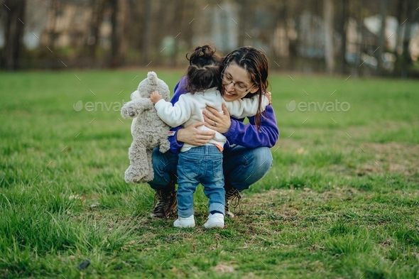 Young millennial mother hugging daughter at park with stuffed animal