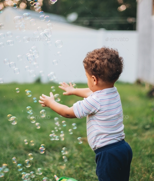 Baby boy at home in backyard playing with bubbles from bubble machine