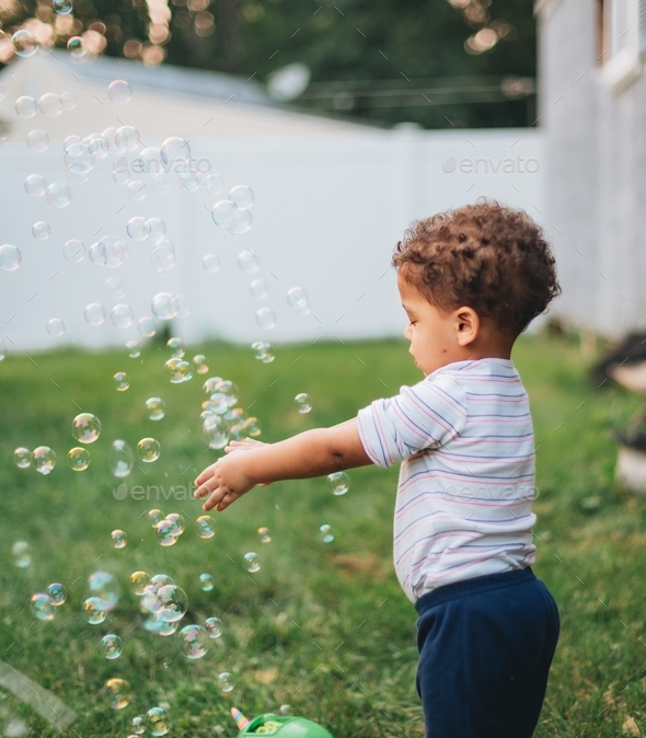 Baby boy at home in backyard playing with bubbles from bubble machine