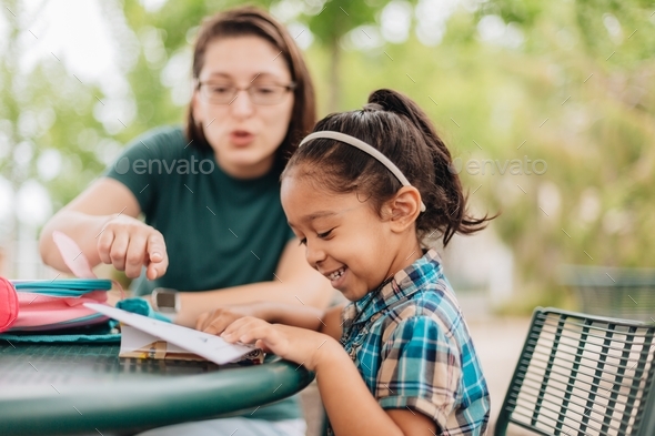 mother and diverse pre school age girl sitting down at table outdoors ...