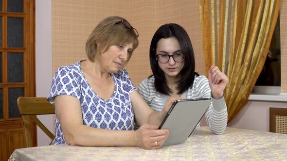 Daughter Teaches Mother How To Use a Tablet. A Young Woman Shows Her Old Mother Where To Click alt
