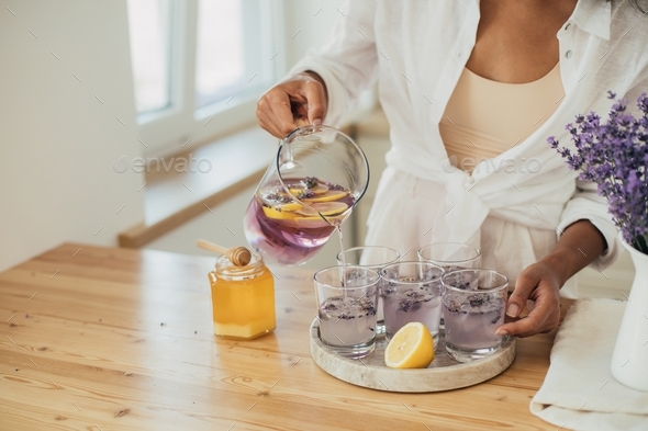 Young woman cooking homemade lavender lemonade using juicer and fresh lemons on a kitchen.