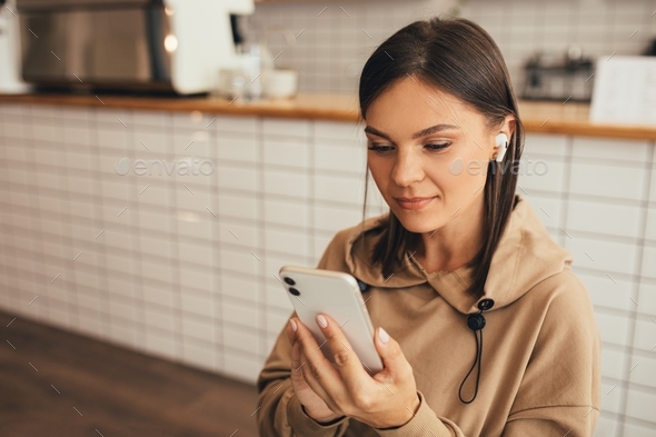 Young woman listening to podcast using wireless Bluetooth earphones and smartphone.