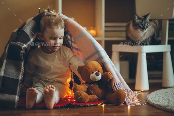 Cute babyplaying in fort made of blankets and garland.