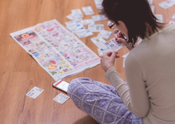 Woman at home clipping coupons from news paper on the floor  - Stock Photo - Images