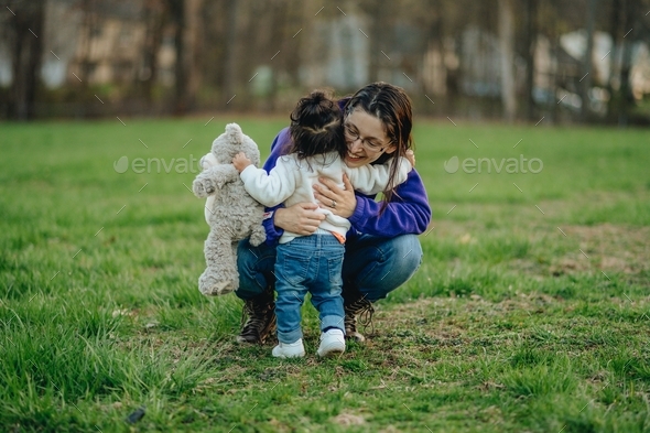 Mother hugging daughter with stuffed animal at park