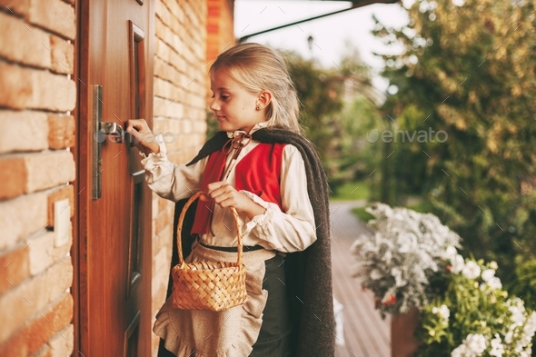 Girl in a fairy costume with a basket in her hands is knocking on the door during the Halloween