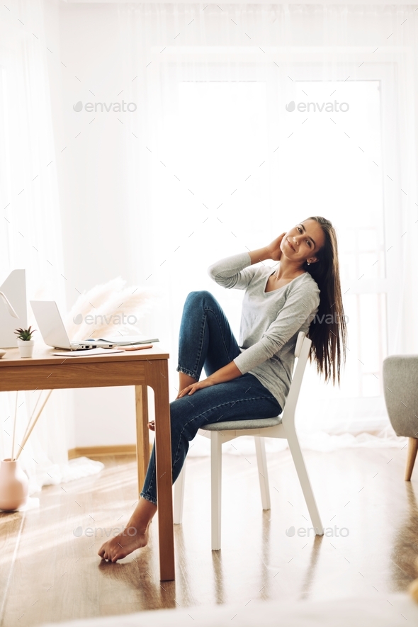 A beautiful girl is sitting leaning back in a chair and stretching after work at a laptop.