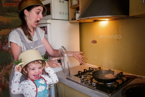Crazy mother with little daughter with saucepans on their heads cheerfully fry cutlets. Funny family