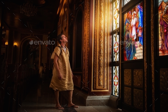 young man tourist stands at painted window in Coptic church in Egypt, looking at the falling light