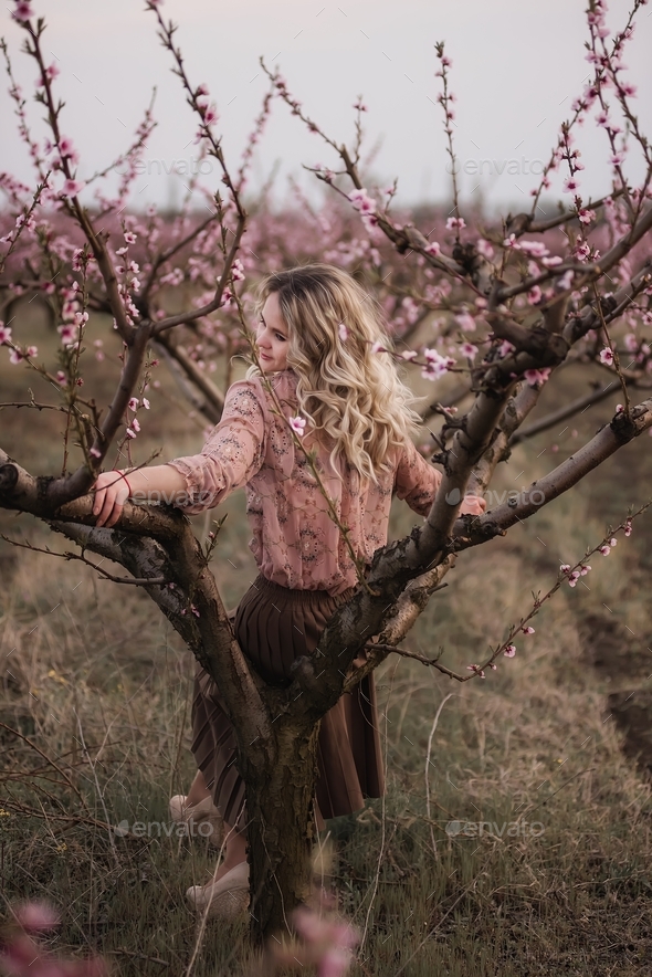 Young beautiful curly blonde woman sits in blooming peach sunset gardens. natural beauty