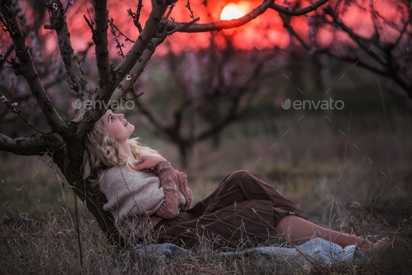 Young beautiful curly blonde woman sits in blooming peach sunset gardens. natural beauty
