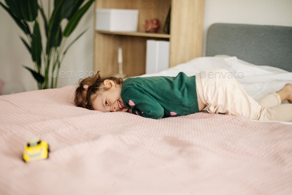 A charming little girl is playing with a car on the bed. Home games, child development - Stock Photo - Images