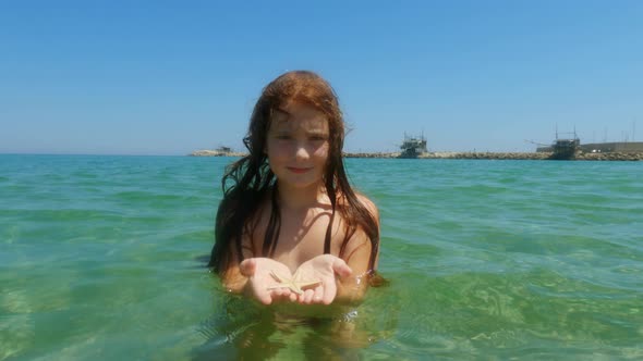 Beautiful adorable redhead child girl bathing in seawater in Italy while holding starfish in hands w alt