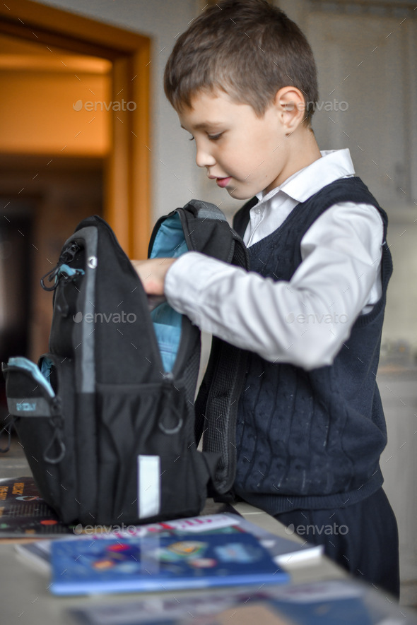 The schoolboy is assembling his knapsack. The student puts textbooks in a backpack - Stock Photo - Images