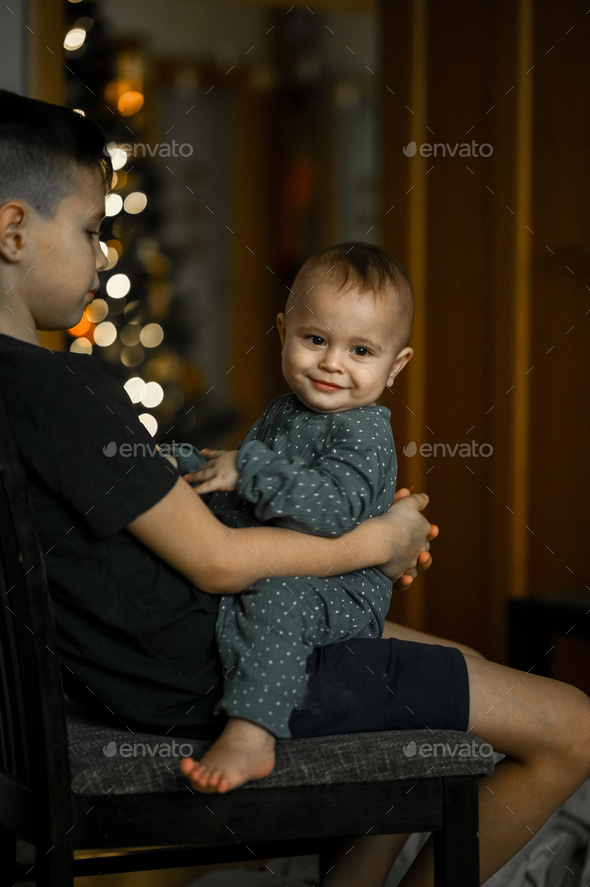 happy children are sitting on a chair against the background of the Christmas tree. - Stock Photo - Images