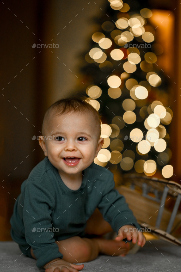 Portrait of a baby against the background of a Christmas tree. The child is crawling at home - Stock Photo - Images