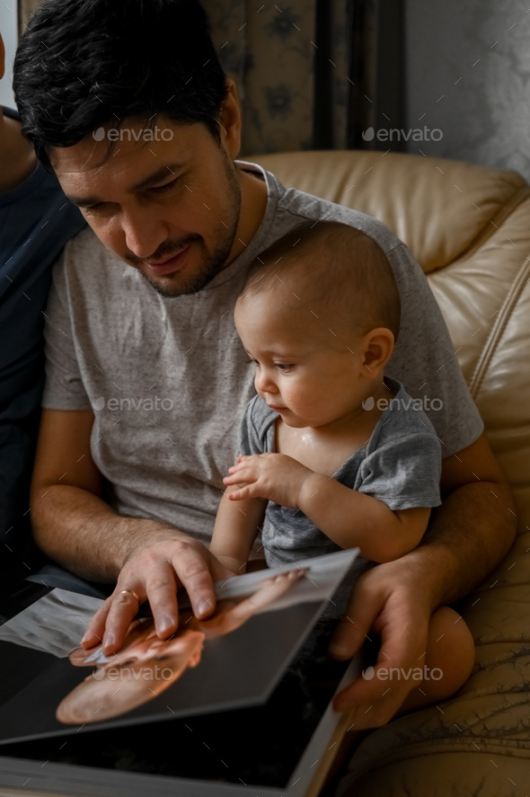 Dad and sons are looking at a family photo album - Stock Photo - Images