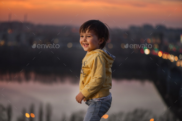 child at sunset on the river against the background of the city - Stock Photo - Images