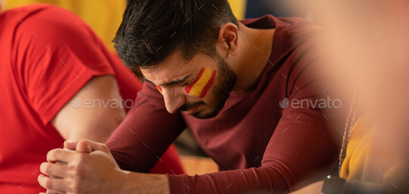 Sad football fan sitting at football stadium, spanish national team in live soccer match.