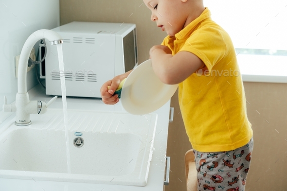 little boy trying to wash the dishes at home