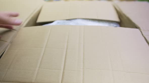 Closeup View of a Caucasian Man is Opening Brown Cardboard Box with Goods Inside