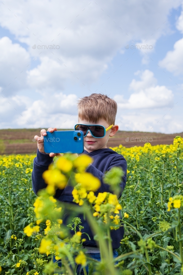 The boy takes pictures of the canola summer landscape on a smartphone. Children using technology - Stock Photo - Images