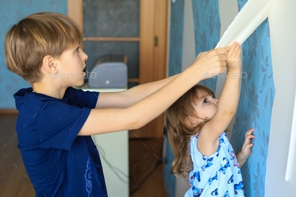 Kids help to make repairs in the apartment, tearing off old wallpaper from the wall