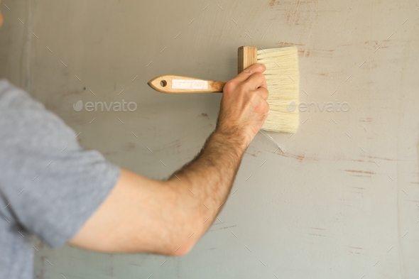 A man makes repairs - he covers the walls with glue by a brush before wallpapering