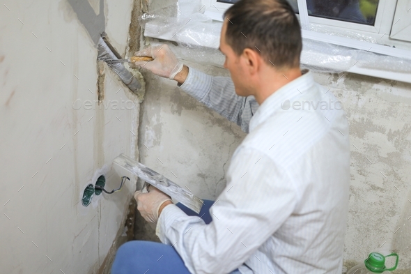 The man covers the wall with mortar with a construction tool. A man makes repairs at home