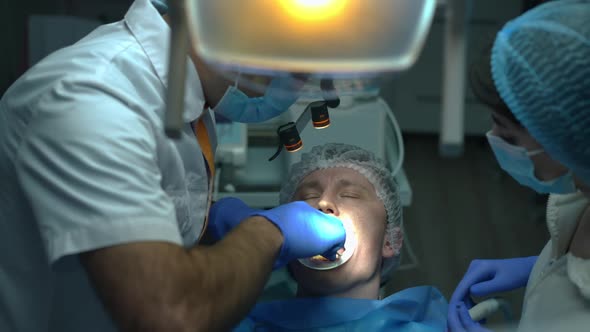 Front View Patient in Dental Chair with Surgeon Sewing Mouth Gum in Slow Motion alt