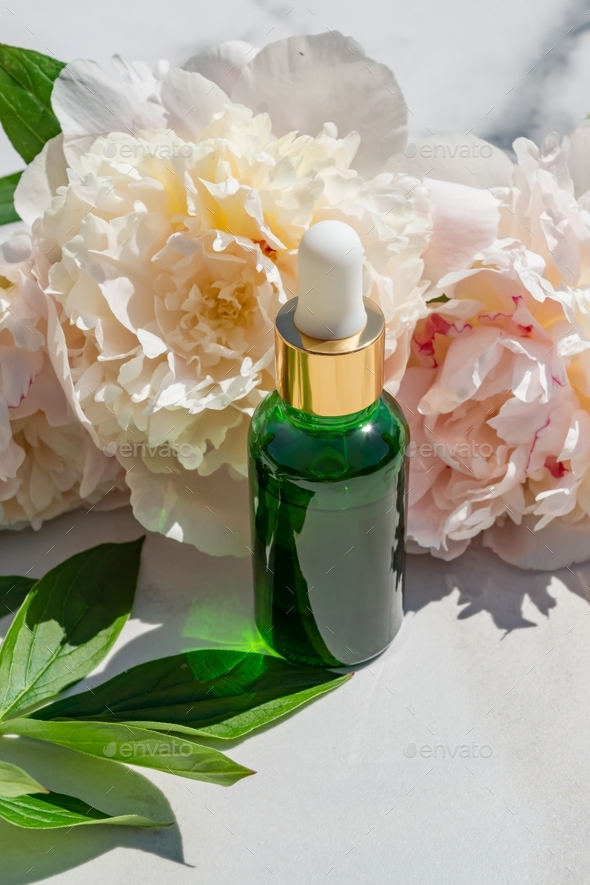 fresh peony flowers and bottle with cosmetic oil on a white marble background with copy space.