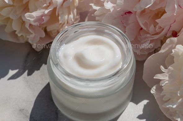 Flowers cosmetic composition with jar of natural face cream and pink blooming peonies on white
