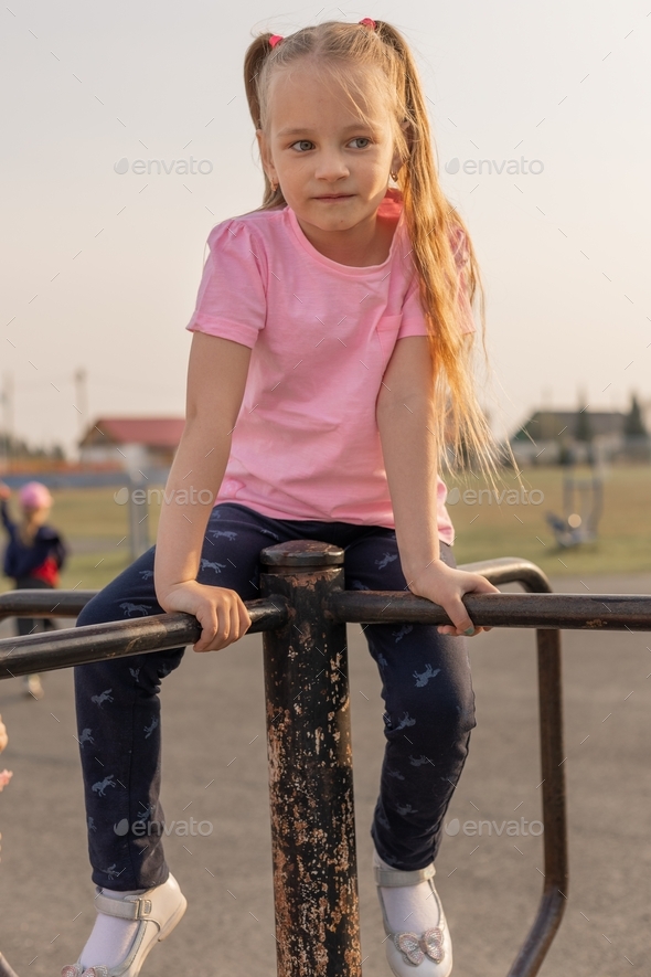 A small child girl with loose hair is spinning on a street horizontal bar at the stadium.