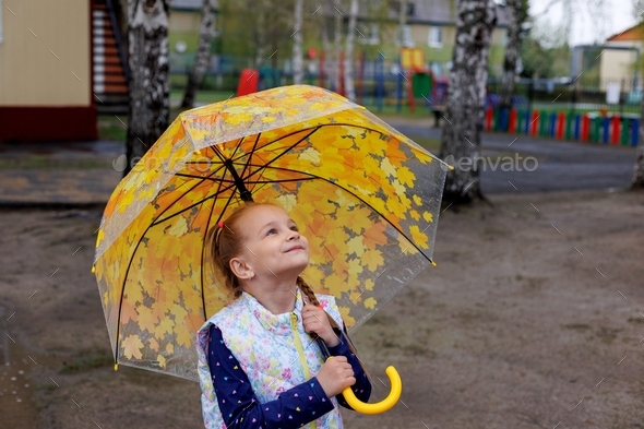 A child girl walks during a light drizzling rain on the street with an umbrella. Spring. Autumn.