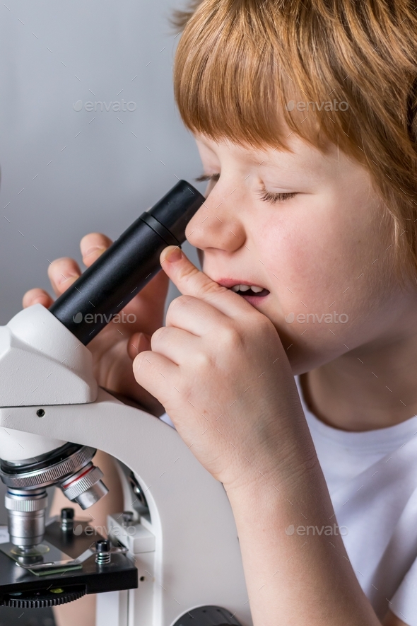 Close-up of a boy\'s face studying glasses with laboratory materials under a microscope